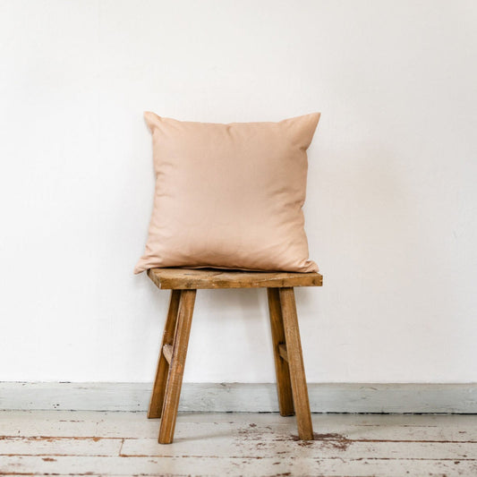 Dekokissen aus rose-beige-farbenem Premium-Samt auf Holzschemel vor weißer Wand.