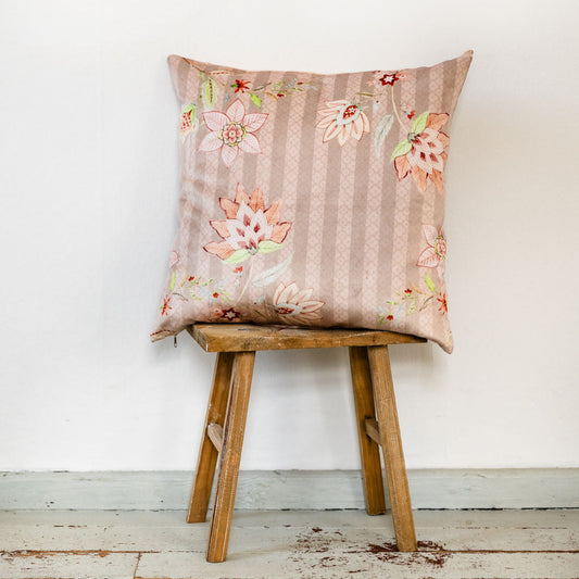 Handgefertigtes Kissen in Rosé-Beige mit floralem Muster aus Premium-Samt, Rückseite gestreift aus Baumwolle, Reißverschluss in Türkis, abgebildet auf einem Hocker vor heller Wand.