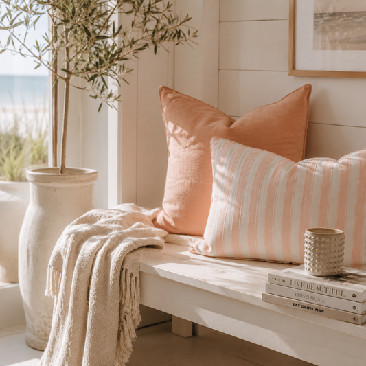 Apricotfarbenes Dekokissen 40x40 kombiniert mit einem gestreiften Kissen auf einer hellen Sitzbank im skandinavischen Landhausstil – stilvolle Deko für Wohnzimmer, Ferienhaus und Ostsee-Ferienwohnung.