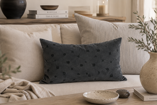 Graphitfarbenes Dot-Kissen aus Premiumsamt von Kissenglück auf einem hellen Sofa. Das unregelmäßige Punktmuster, inspiriert von einer vergrößerten Struktur eines Schwalbenflügels, wird mit Leinenkissen und feinen Streifen zu einer ruhigen skandinavischen Wohnkombination ergänzt.