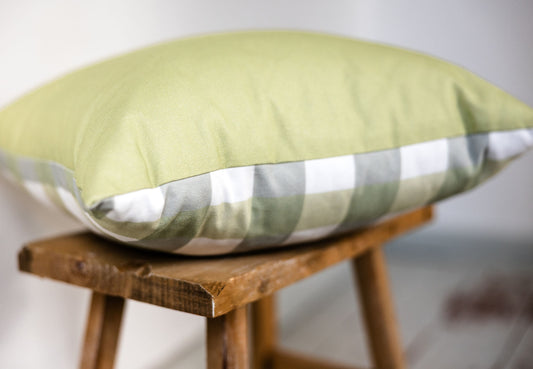 Detailansicht des karierten Kissens mit unifarbener Rückseite in Grün und Karomuster in Weiß, Grün und Graublau auf Holzschemel