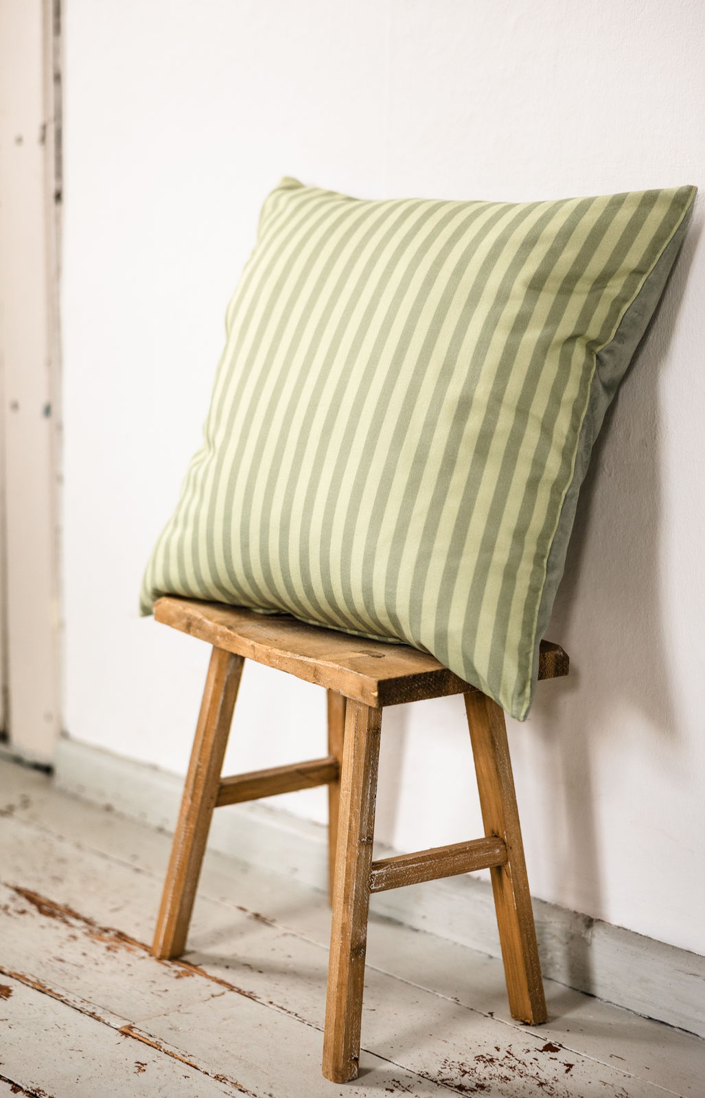 Quadratisches Kissen mit grün-grünem Streifenmuster auf einem Hocker an weißer Wand, skandinavisch schlichtes Interior
