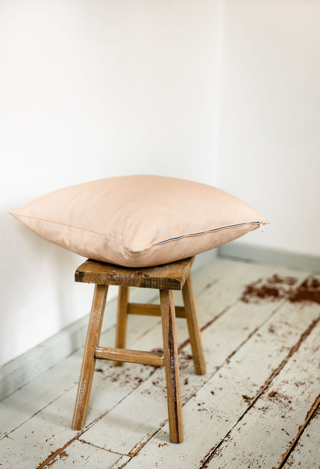 Rose-Beige-farbenes Samtkissen im Querformat auf Hocker – mit sichtbarem türkisfarbenem Reißverschluss als farbigem Akzent.