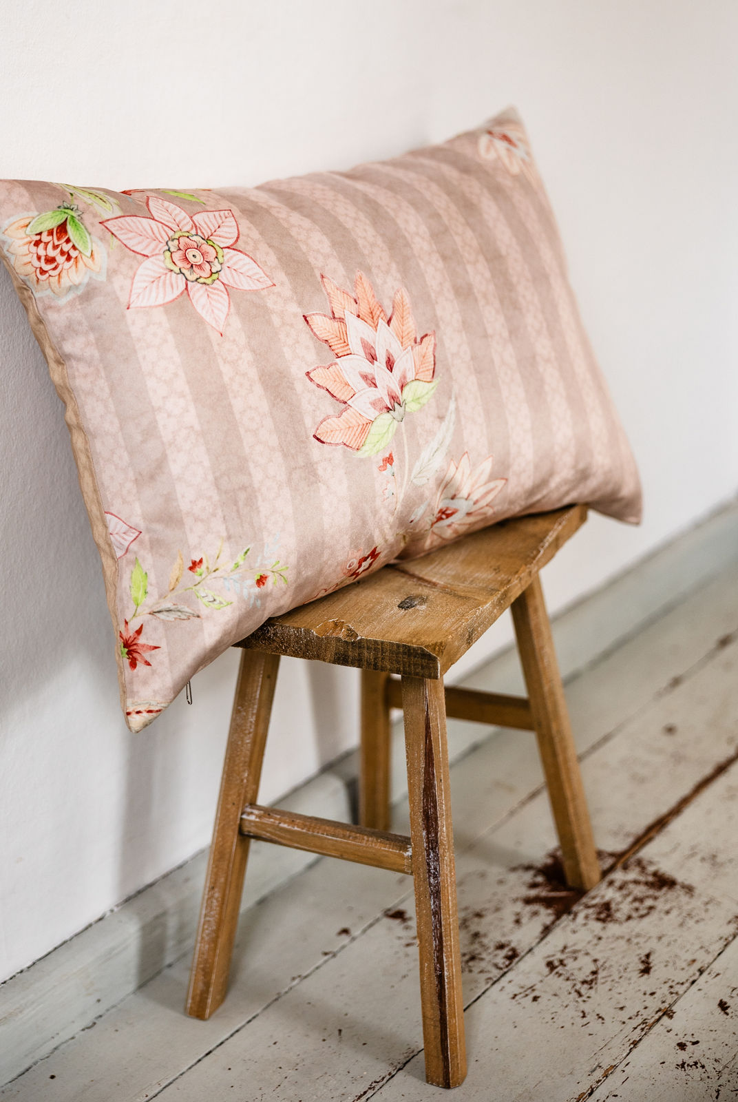 Rosé-beiges Zierkissen mit floraler Stickerei auf gestreiftem Premium-Samt, im Maß 40 × 60 cm auf Holzschemel vor weißer Wand drapiert