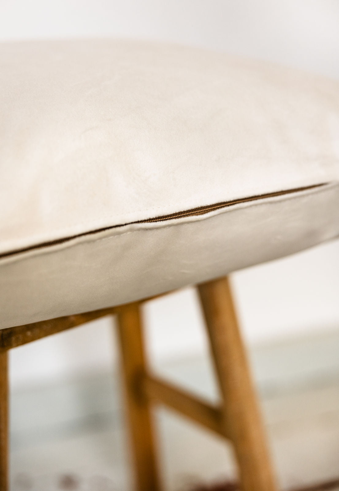 Detailaufnahme eines Kissens in Soft White aus Premium-Samt mit dezentem, farblich abgestimmtem Reißverschluss auf Holzschemel