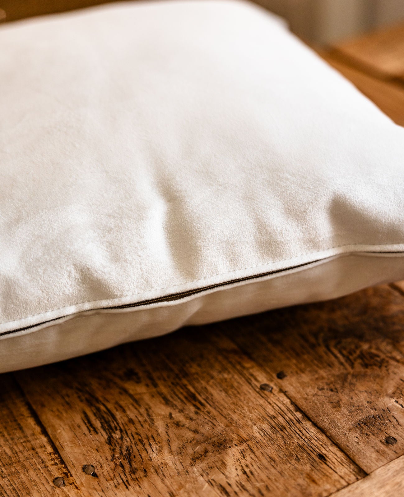  Detailansicht des Soft White Kissens aus Premium-Samt mit farblich passendem Reißverschluss, liegend auf Holztisch