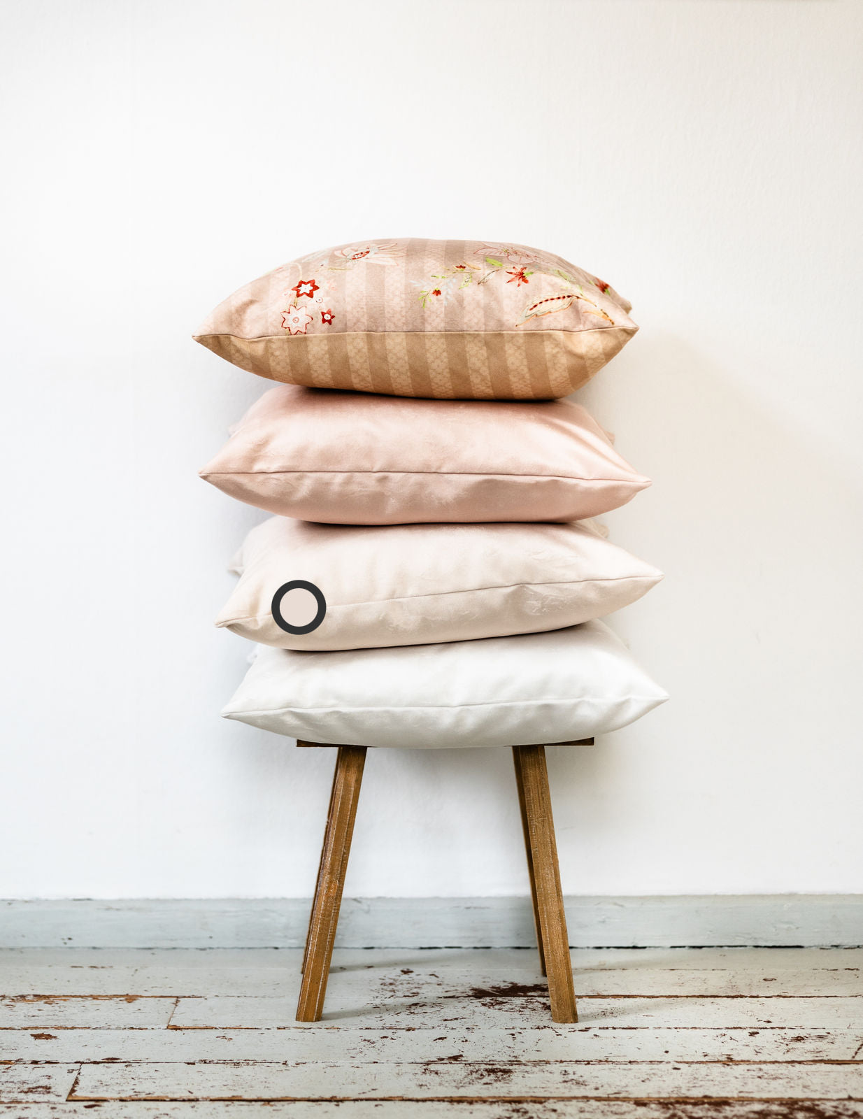 Vier handgefertigte Premium-Samtkissen im Farbspektrum Rosé-Beige, Rosé, Beige und Weiß – als dekorativer Kissenstapel auf einem Holzschemel arrangiert.