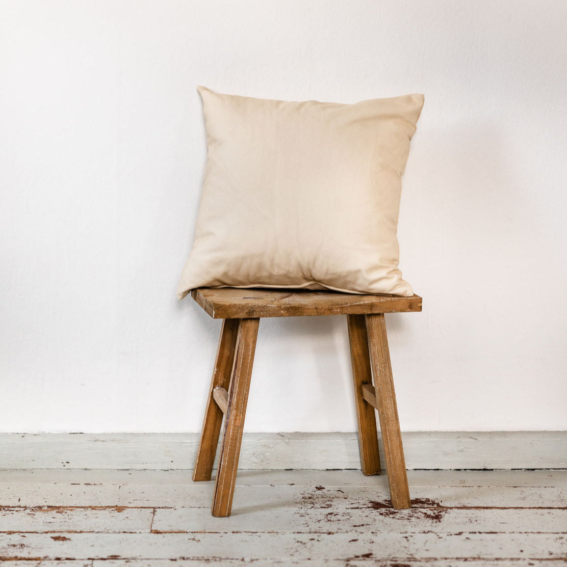 Beige Kissenhülle aus Baumwolle auf rustikalem Hocker, schlicht und natürlich, 50 × 50 cm