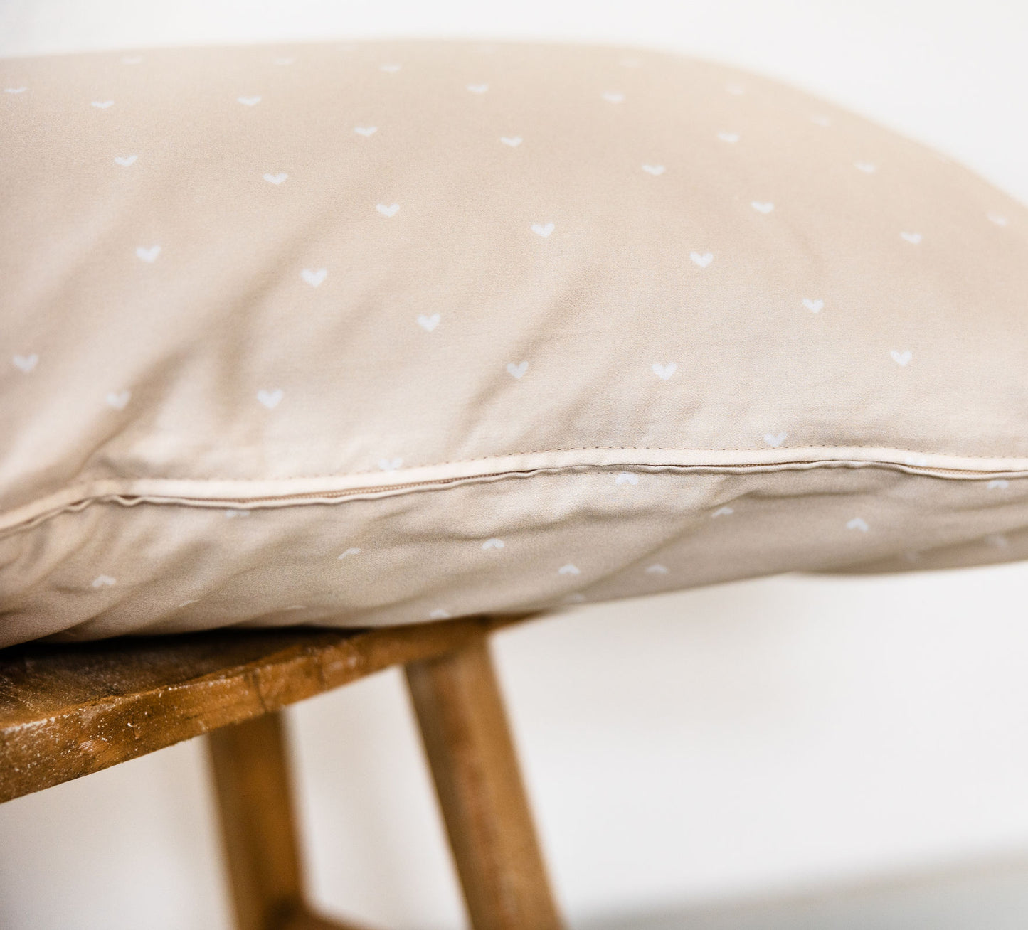 Bettkissen in Beige, 80x40 cm, aus weichem Baumwoll-Perkal mit zartem Herzmuster, dekorativ auf einem Holzstuhl arrangiert.
