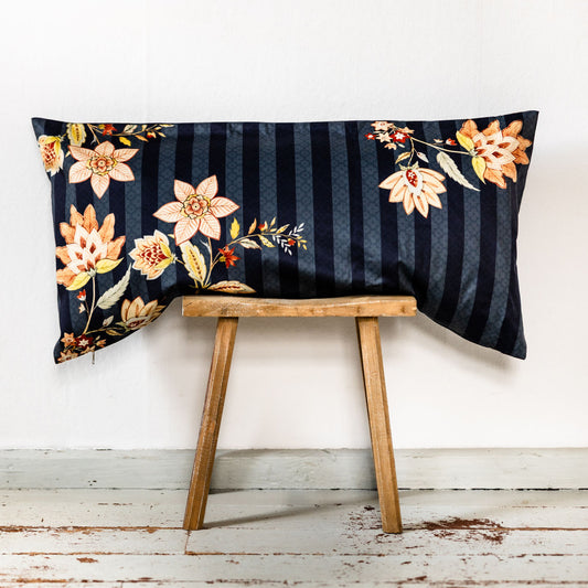  Rechteckiges Bettkissen in 40x80 cm aus dunkelblauem Baumwollperkal mit Ton-in-Ton Streifen und floralem Muster in warmen Gelb-, Orange- und Rottönen, auf einem rustikalen Holzstuhl vor weißer Wand platziert.