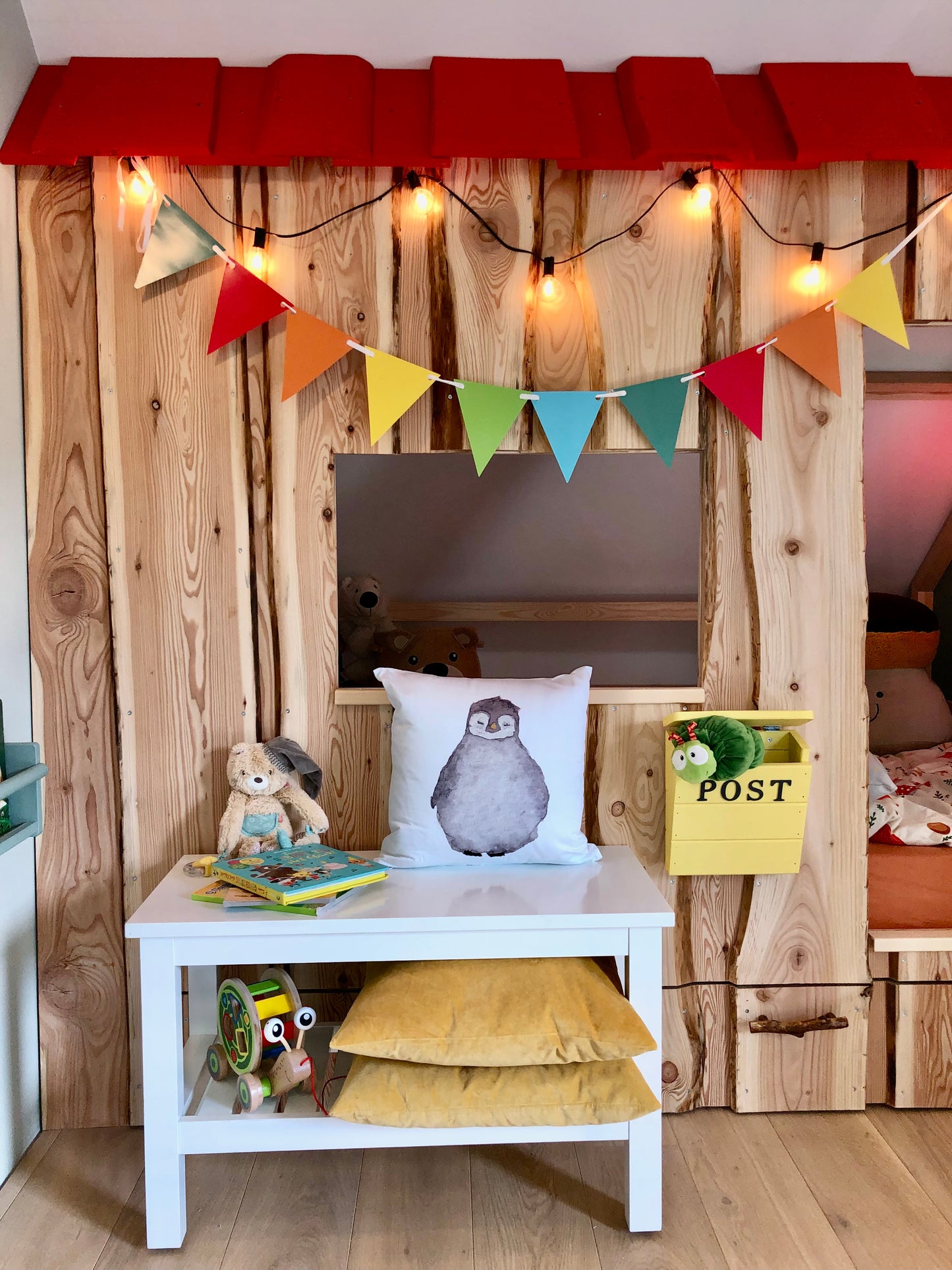 Kinderzimmer mit Hüttenbett aus Holz. Davor steht eine weiße Bank auf der einKinder Dekokissen steht. Auf dem Kissen ist ein süßer Pinguin zu sehen. Der Pinguin ist handgezeichnet. Aquarell.