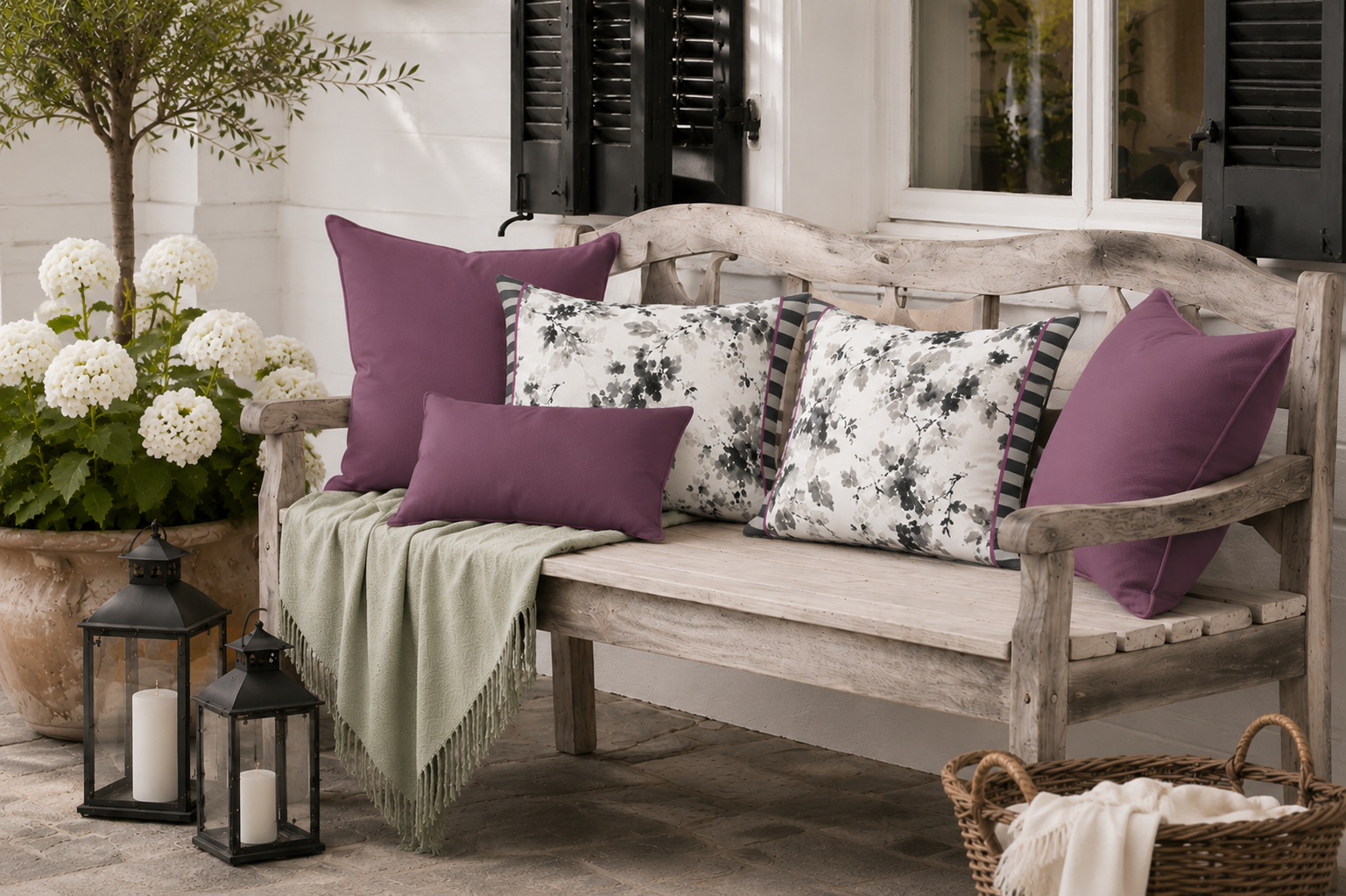 Dekokissen-Kombination aus Aubergine, Anthrazit und floralen Kissen in Grau-Weiß auf einer rustikalen Gartenbank. Elegante Outdoor-Kissen für Landhausgarten, Terrasse und gemütliche Sitzplätze im Freien.